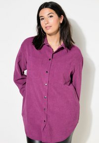 Camicia viola con bottoni, colletto, due tasche sul petto e maniche lunghe. Realizzata in tessuto testurizzato, con bottoni neri e orlo curvo.