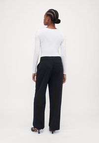 White long-sleeve top paired with high-waisted black trousers. The trousers have a straight cut. Black heels complete the outfit.