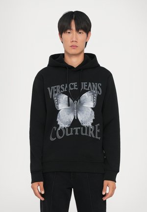 Felpa nera in cotone con una grande grafica di una farfalla grigia e la scritta "VERSACE JEANS COUTURE". Dotata di cappuccio con cordino e polsini a costine.