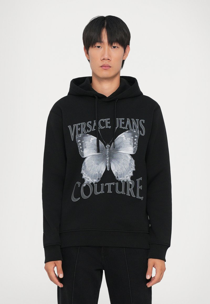 Hanorac din bumbac negru, cu un grafic mare de fluture gri și textul "VERSACE JEANS COUTURE". Proiectat cu un glugă cu șnur și manșete ribbed.