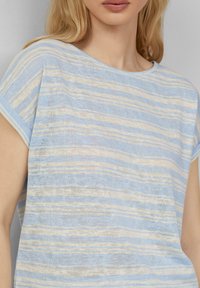 Lichtblauw gestreept topje van zachte, gestructureerde stof met afwisselend witte en beige strepen, ronde halslijn en korte mouwen.