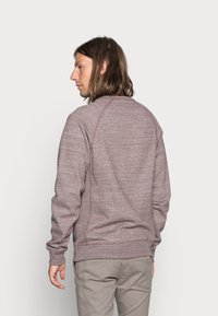 Sudadera burdeos con un acabado texturizado, mangas raglán y costuras de contraste. Presenta un cuello redondo y puños acanalados.