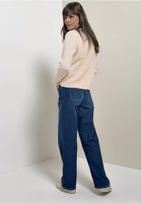 Lichtroze, fluffy trui en losse blauwe jeans, gecombineerd met witte sneakers. De outfit toont een casual, comfortabele stijl.