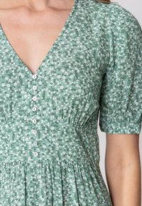 Green floral dress with puffed sleeves and a V-neck. Features a button-down front and a gathered waist with a flowy skirt.
