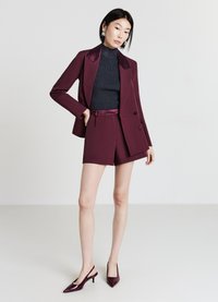 Blazer bourgogne avec revers en satin, shorts assortis et un haut texturé foncé. Associé à des escarpins bourgogne à bout pointu et à talon ouvert.