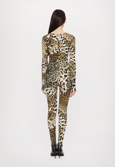Kompletna obleka z leopardjim vzorcem, dolgimi rokavi, ki vključuje mešanico zlatih, črnih in rjavih tonov ter prilagojen kroj. Črne škornje na peto.