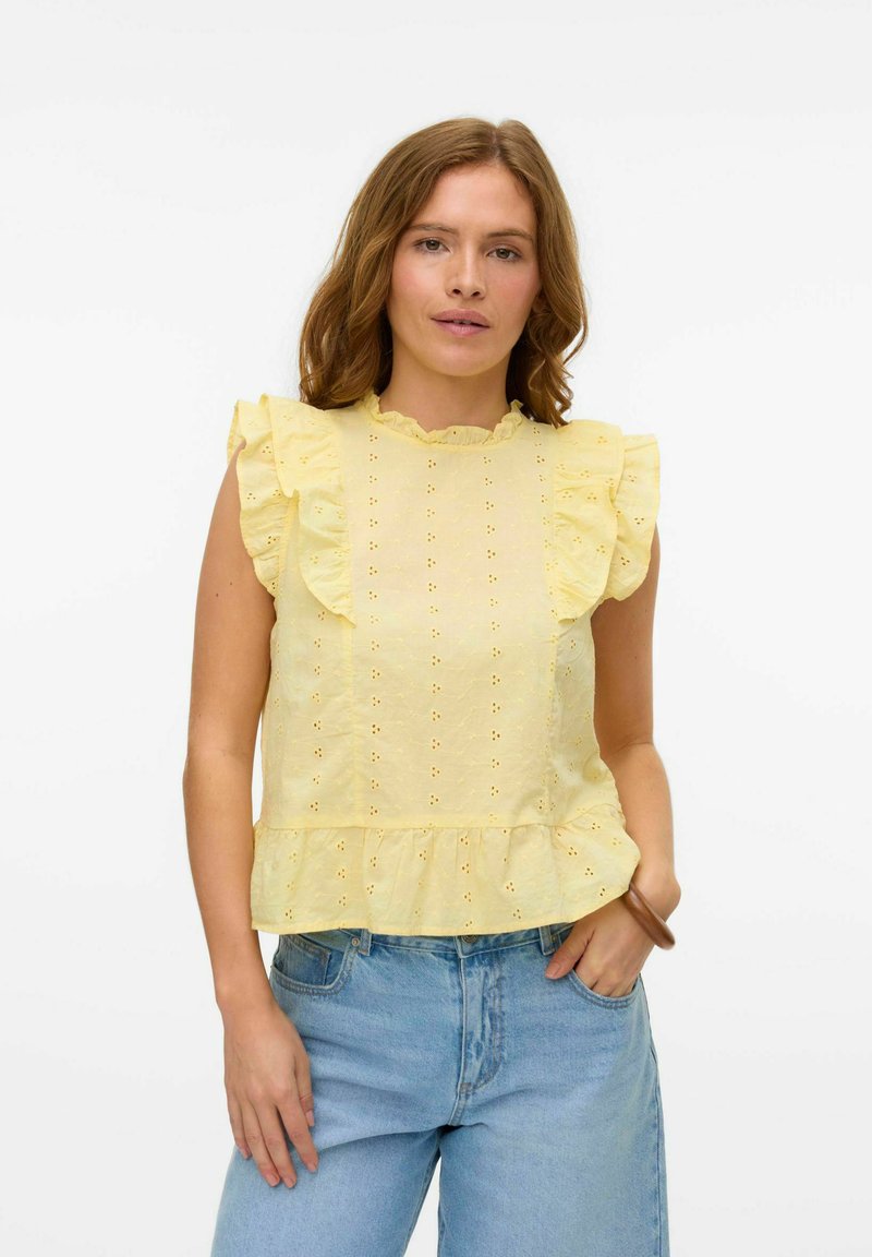 Top giallo con peplum, maniche a volant, motivo ad occhiello e scollatura arricciata. Abbinato a jeans di denim blu chiaro.