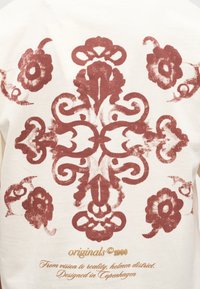 Ruosteenvärinen symmetrinen kukkakuvio ja rullaaiheinen kuvio valkoisella kankaalla, jossa kullankeltainen teksti "originals © 1990" ja "Designed in Copenhagen."