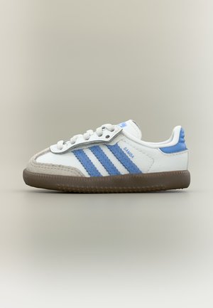 Fehér és kék Adidas Samba sportcipő barna talppal, fehér fűzőkkel és kék sarkal részlettel, oldalnézetből, semleges háttér előtt.