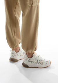 Weiße Sneakers mit strukturierten Akzenten, kontrastierender grauer Sohle und Schnürsenkeln. Kombiniert mit beigefarbenen, mit Gummizug versehenen Hosen für eine lässige Passform.