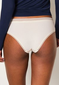 Mutande beige a coste con bordo in pizzo ondulato in vita, modellate per una copertura perfetta, abbinate a una maglietta a maniche lunghe blu navy.