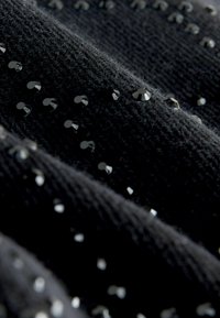 Czarna tkanina o teksturze z rozproszonymi, fasetowanymi czarnymi cekinami, które nadają subtelny blask. Tkanina wydaje się miękka i nieco puszysta.