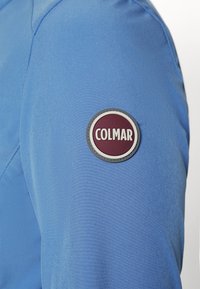 Blue fabric sleeve featuring a round logo patch with a dark red background and white text reading "COLMAR." Smooth texture, fitted design.