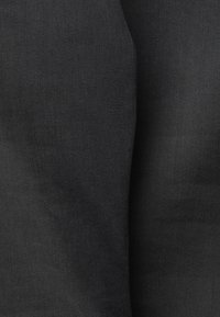 Gros plan sur un tissu noir avec une texture fine visible et des plis subtils créant des ombres et des reflets.