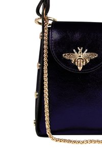 Zwarte en paarse glanzende leren handtas met een gouden bij-embleem op de klep, een decoratieve gouden kettinghengsel en metallic accenten aan de zijkant.