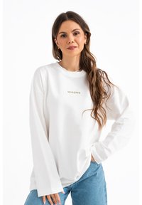 Felpa bianca oversize con maniche lunghe, caratterizzata da un sottile logo 'MIRONS' in verde. Tessuto morbido; vestibilità comoda; design minimal.