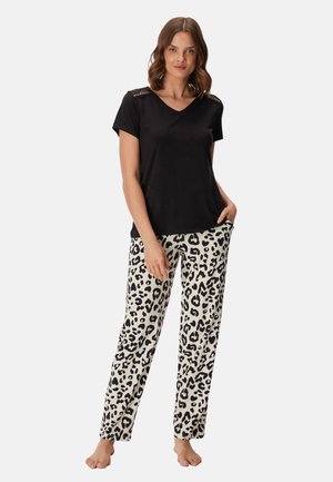 Donna in piedi a piedi nudi che indossa una maglietta nera a maniche corte con dettagli in pizzo e pantaloni bianchi con motivo leopardato nero.