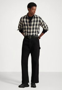 Czarna i biała koszula w kratę z długimi rękawami, zestawiona z luźnymi czarnymi spodniami i czarnymi trampkami. Strój posiada pasek i podwinięte mankiety.