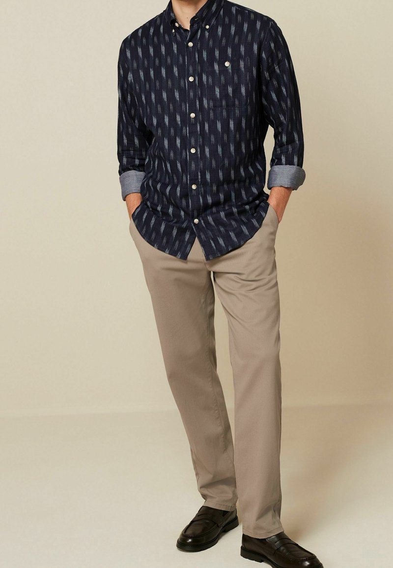 Marineblauwe overhemd met knopen, met een geometrisch patroon, opgerolde mouwen, lichtkhaki broek en zwarte instappers. Subtiele texturen en contrastdetails.