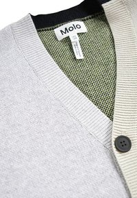 Ljusgrå cardigan med en mörkgrön texturerad insida. Har en ribbad krage och manschetter, samt en svart knappstängning.