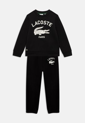Zwarte sweatshirt en broek set met wit Lacoste-logo en krokodilafbeelding op de borst en linkerdij, ontworpen voor casual draag.