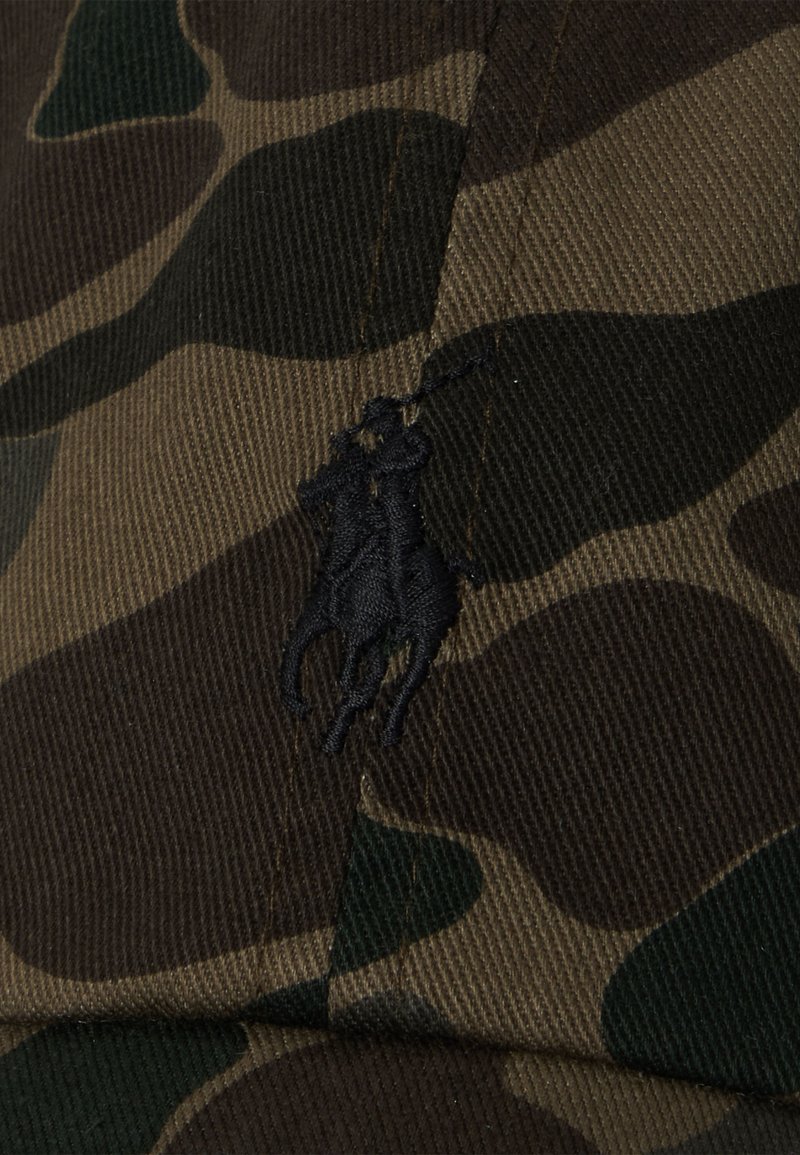 Camo-musterte Kappe aus Stoff in verschiedenen Grüntönen und Brauntönen. Schwarzes gesticktes Logo eines Pferdes mit Reiter auf der Vorderseite.