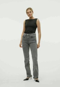 Μαύρη αμάνικη μπλούζα συνδυασμένη με ψηλόμεσα παντελόνια γκρι ριγέ, τονισμένα από εφαρμοστή σιλουέτα και κομψές μαύρες γόβες.