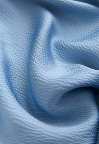 Tissu bleu clair avec un motif texturé en forme de gaufre, présenté en gros plan avec de légers plis et des ombres douces.