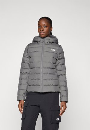 Grijze pufferjack met een capuchon, voorzien van gestikte secties, een rits aan de voorkant en het North Face-logo op de linkerborst.