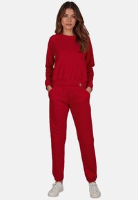 Rode sweater en bijpassende joggingbroek, beide van een zacht materiaal. Sweater heeft een ronde hals en een geribbelde zoom, de joggingbroek heeft zijzakken en elastische boorden.