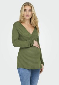 Olijfgroen zwangerschapsshirt met ribbeltextuur, V-hals en lange mouwen, gecombineerd met lichtblauwe jeans. Eenvoudig, casual ontwerp.