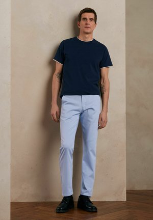Granatowa koszulka z białymi wykończeniami, jasnoniebieskie spodnie i czarne buty. Styl jest casualowy; spodnie są zwężane, a koszulka ma okrągły dekolt.