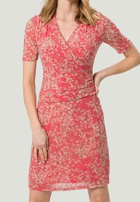 Kukallinen kietaisumekko vaaleanpunaisena, jossa on lyhyet hihat. Mekossa on istuva siluetti, pehmeä kangas ja hienovarainen kukkakuosi.