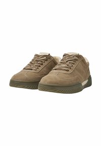 Brown suede sneakers with a textured finish, featuring a cream-colored tongue and contrasting laces, set on a thick rubber sole.