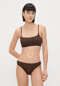 Rjav modrček in ujemajoče se bikini, ki imata subtilen vzorec listov. Material je gladek, z tankimi naramnicami in elastičnim pasom.