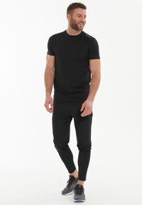 Sort atletisk T-shirt med korte ærmer, lavet af et glat stof. Kombineret med sorte tapered bukser med slim fit og elastisk talje.