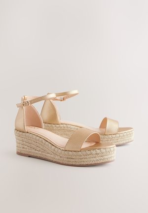 Sandaletter med kilehæl i guldfarvet tonet materiale med ankelrem, der har en tekstureret overdel og flettet jute-platform. Åben tå og glat fodseng.