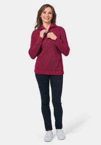 Bordeaux gebreide trui met een hoge kraag, voorzien van diagonale ribbels en een losse pasvorm, gedragen met donkere jeans en witte sneakers.