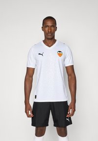Hvit fotballtrøye med teksturert mønster, Valencia CF-logo og svarte Puma-detaljer, sammen med sorte shorts og hvite sokker.