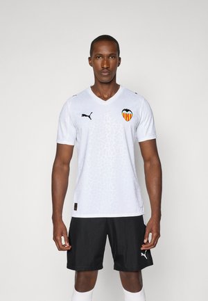 White soccer jersey features a textured pattern, Valencia CF logo, and black Puma accents, paired with black shorts and white socks.