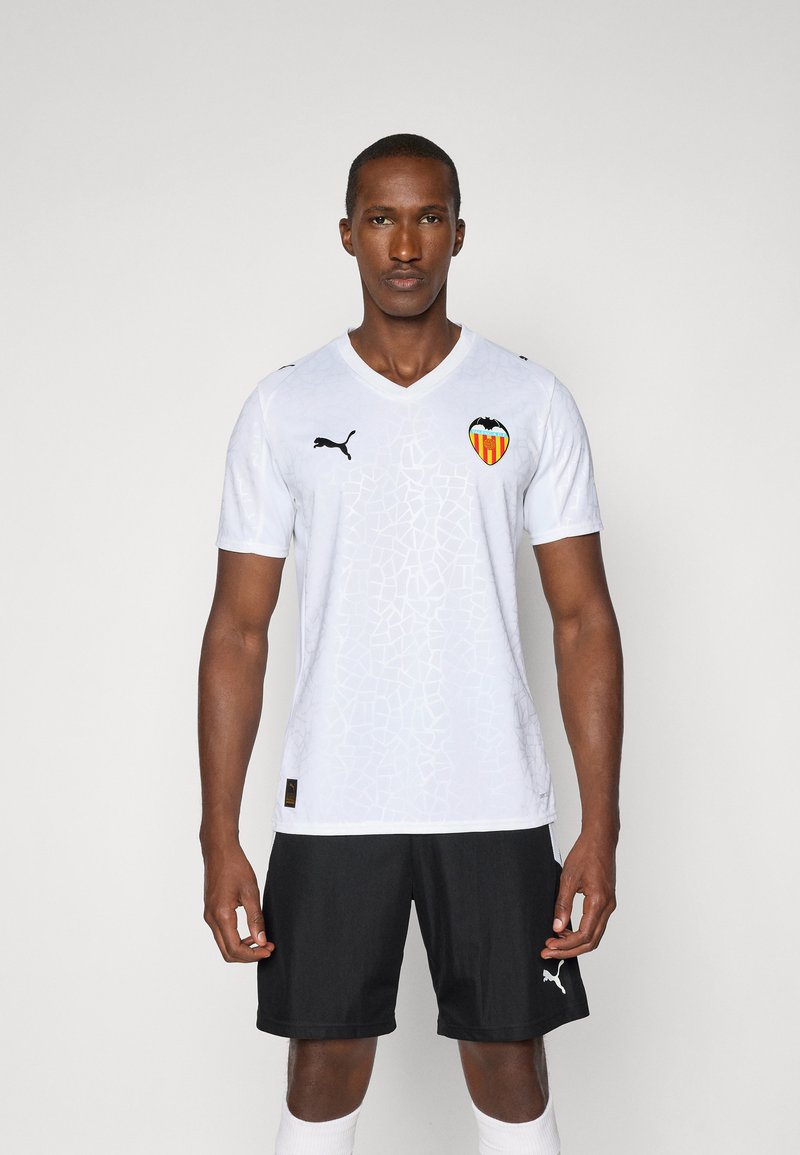 Hvit fotballtrøye med teksturert mønster, Valencia CF-logo og svarte Puma-detaljer, sammen med sorte shorts og hvite sokker.