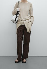 Beige gebreide trui over een wit shirt, bruine wijde broek en zwarte flip-flops. Een kleine handtas in zwart-wit patroon complementeert de outfit.