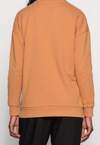 Sudadera naranja de tejido suave, con cuello redondo y mangas largas, con un corte relajado y puños y dobladillo acanalados.