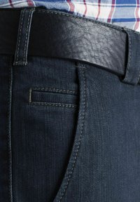 Jean en denim bleu foncé avec une ceinture en cuir noire. Comprend une poche latérale et des coutures contrastées le long des coutures. Accent en cuir texturé.