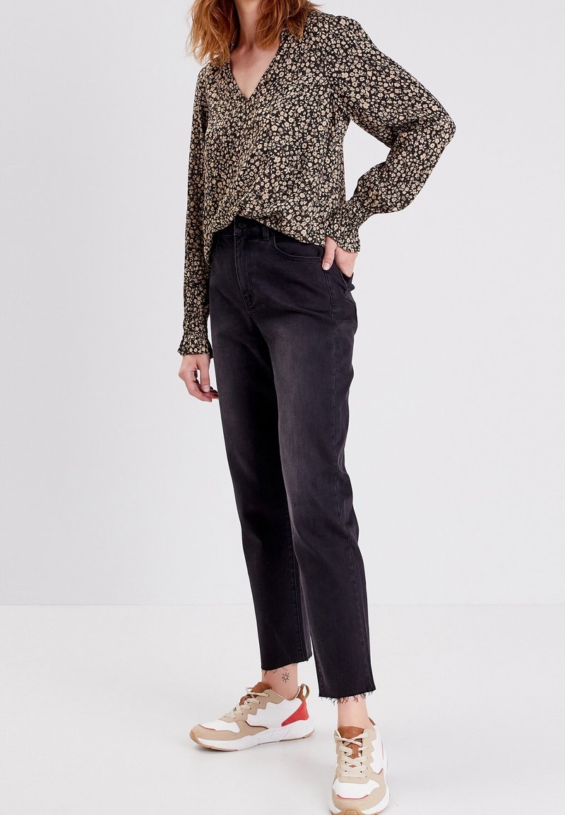 Jean noir taille haute associé à un chemisier noir à imprimé floral avec un col en V et des manches longues. La tenue est complétée par des baskets sportives.