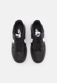 Svarta lädersneakers med en texturerad yta, vita Nike-swoosh-accenter, svarta snören och en rundad tådesign.