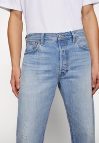 Ljust blå slitna jeans med en klassisk passform, featuring en knappstängning, femficksdesign och subtila sömnadsdetaljer.