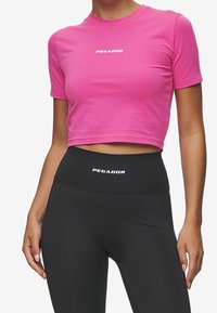 Roze cropped t-shirt met korte mouwen en een witte 'PEGADOR' logo. Gemaakt in combinatie met hoge zwarte leggings met hetzelfde logo.