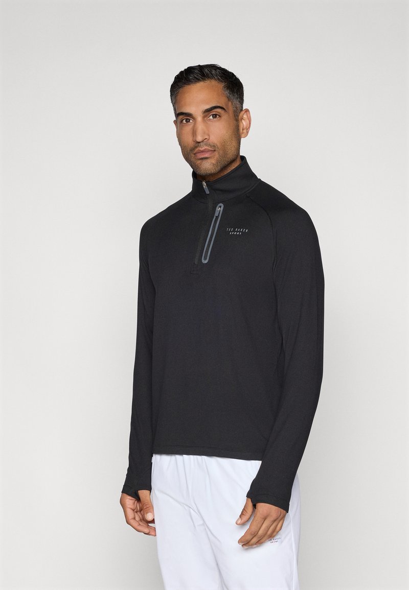 Tricou negru cu mânecă lungă, tip fermoar, având un guler înalt și un fermoar parțial. Material neted cu un logo subtil în gri închis.