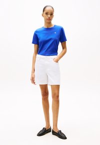 Blå bomulls t-skjorte med korte ermer, hvite denimshorts og svarte loafers. antrekket har et enkelt design med en klassisk passform.